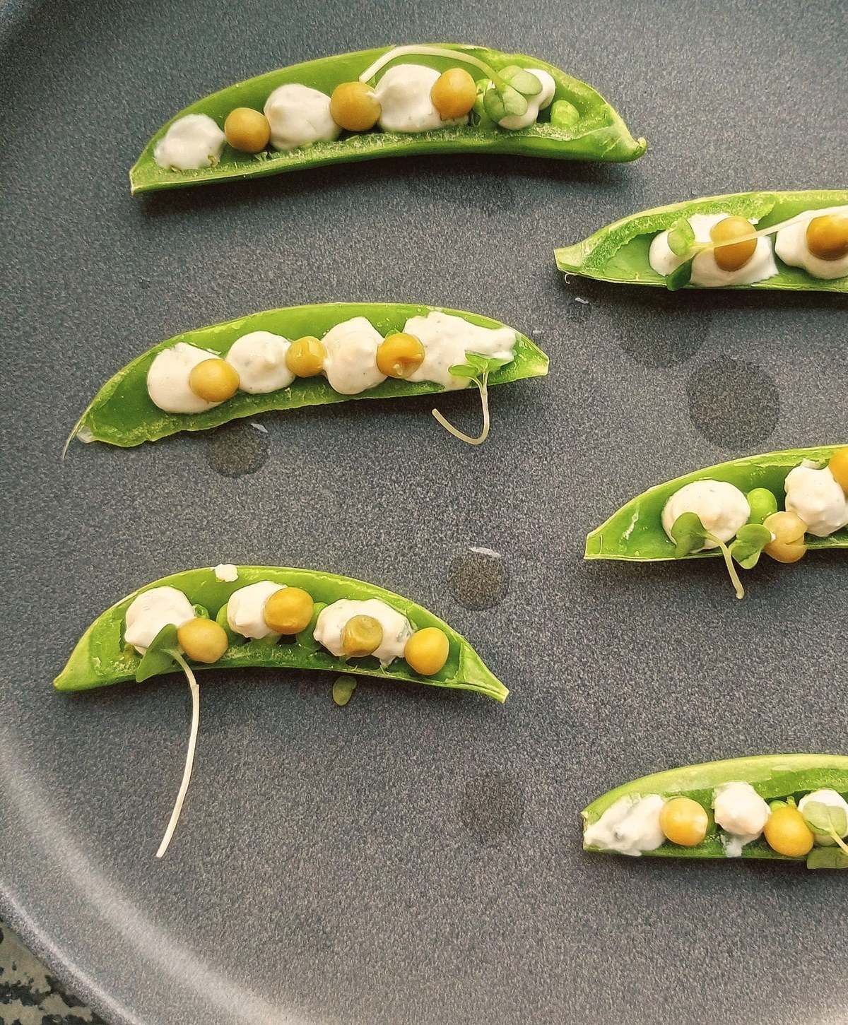 Pea pods filled with peas and cream, on a slate plate.