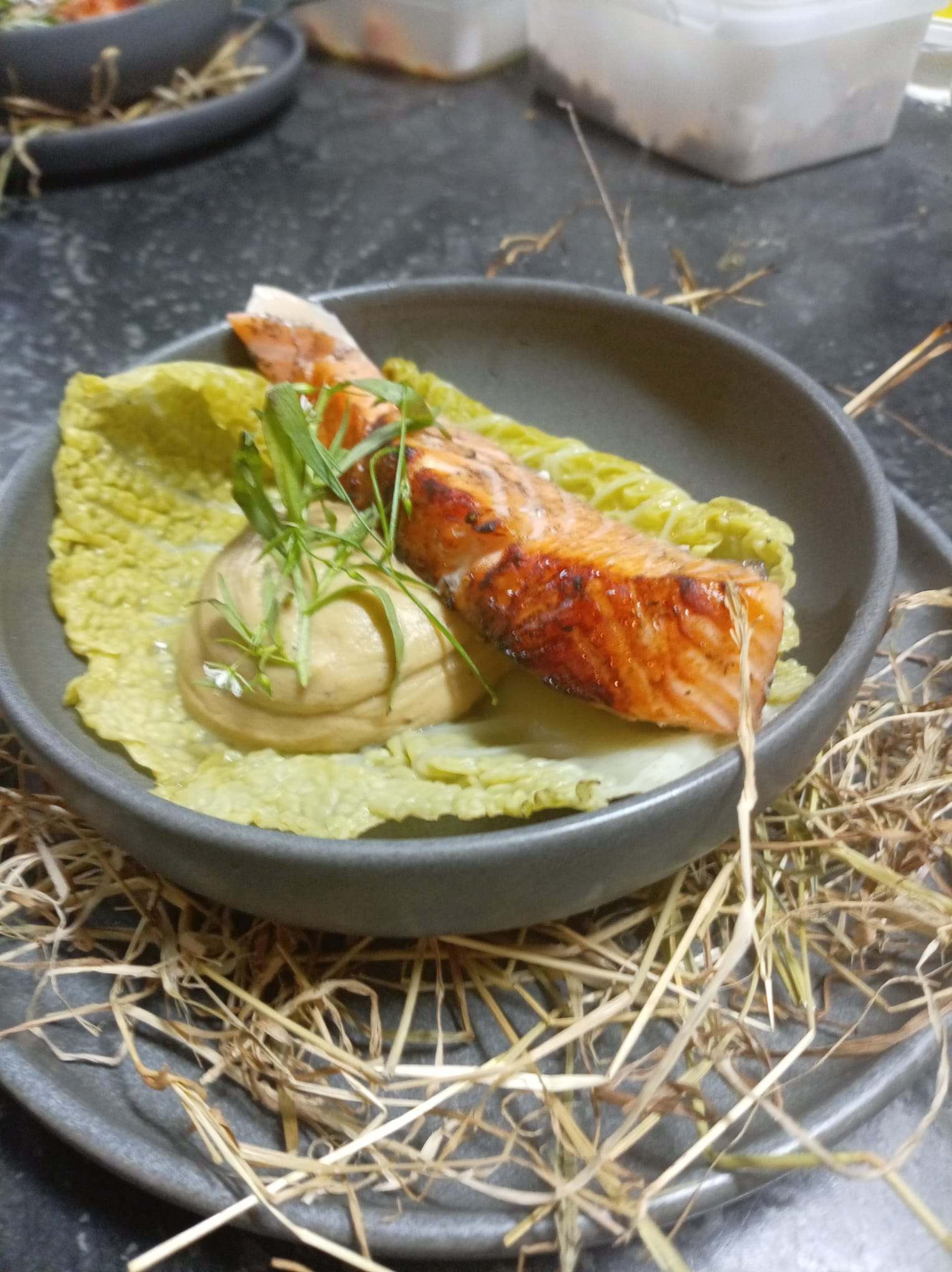 Glazed salmon on a cabbage leaf with a quenelle of cream and herbs, served on hay.